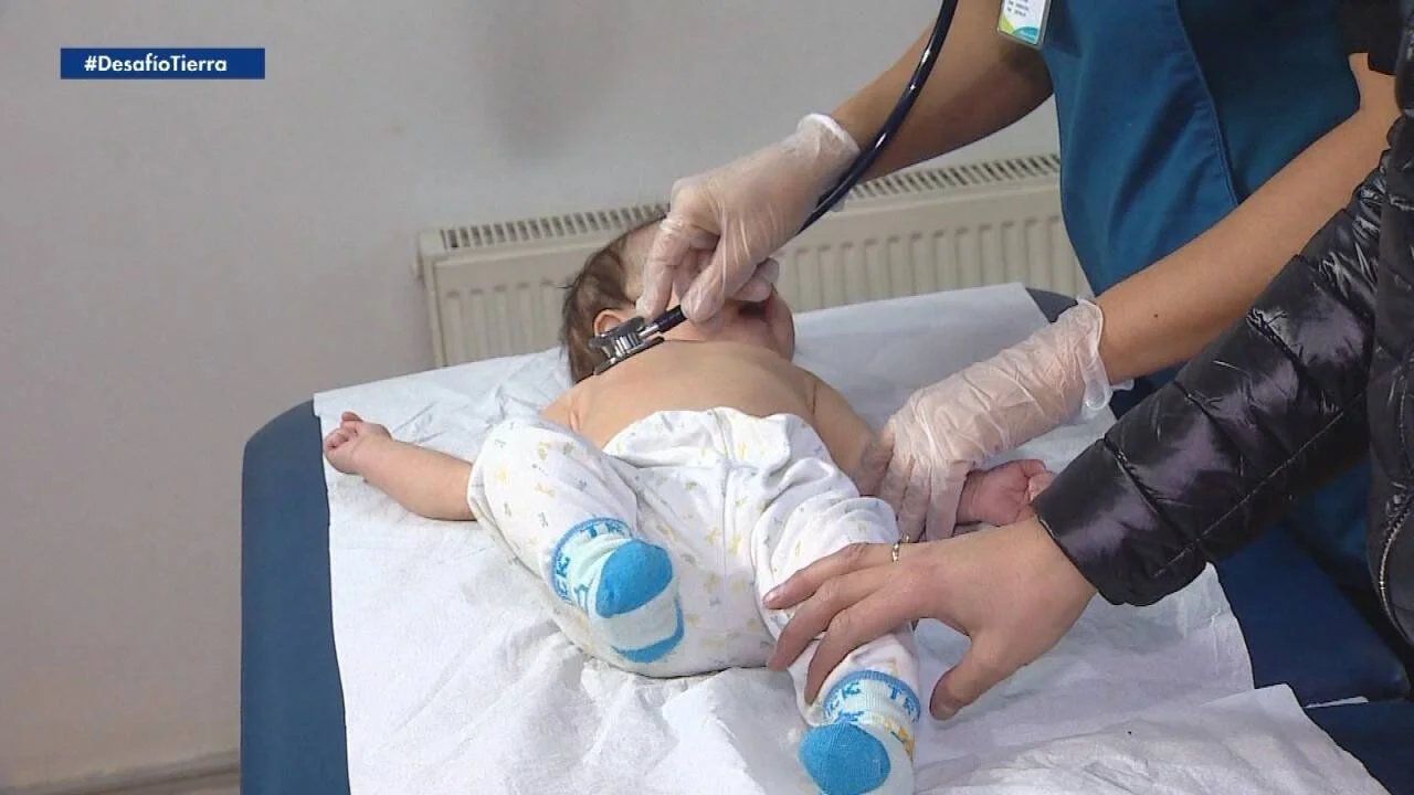 Profesional de salud con guantes ausculta a un bebé acostado en una camilla durante una revisión médica.