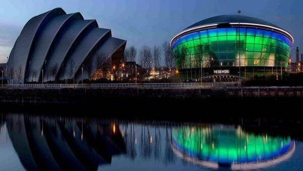 El SEC Armadillo y el SSE Hydro de Glasgow iluminados de noche, reflejados en el río Clyde.