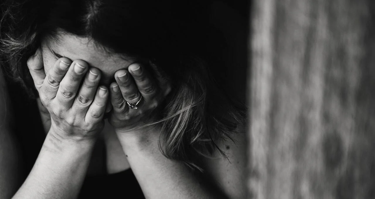 Mujer con anillo cubre su rostro con ambas manos en actitud de llanto o angustia, fotografía en blanco y negro.