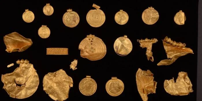 Conjunto de medallones, monedas y fragmentos de oro antiguo dispuestos sobre superficie negra, parte de un hallazgo arqueológico.