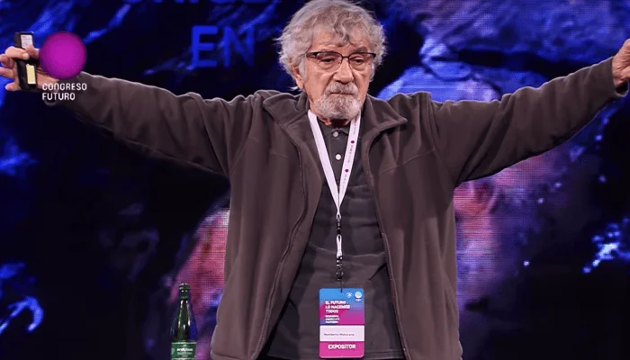 Hombre mayor con credencial de expositor abre los brazos en el escenario del Congreso Futuro.