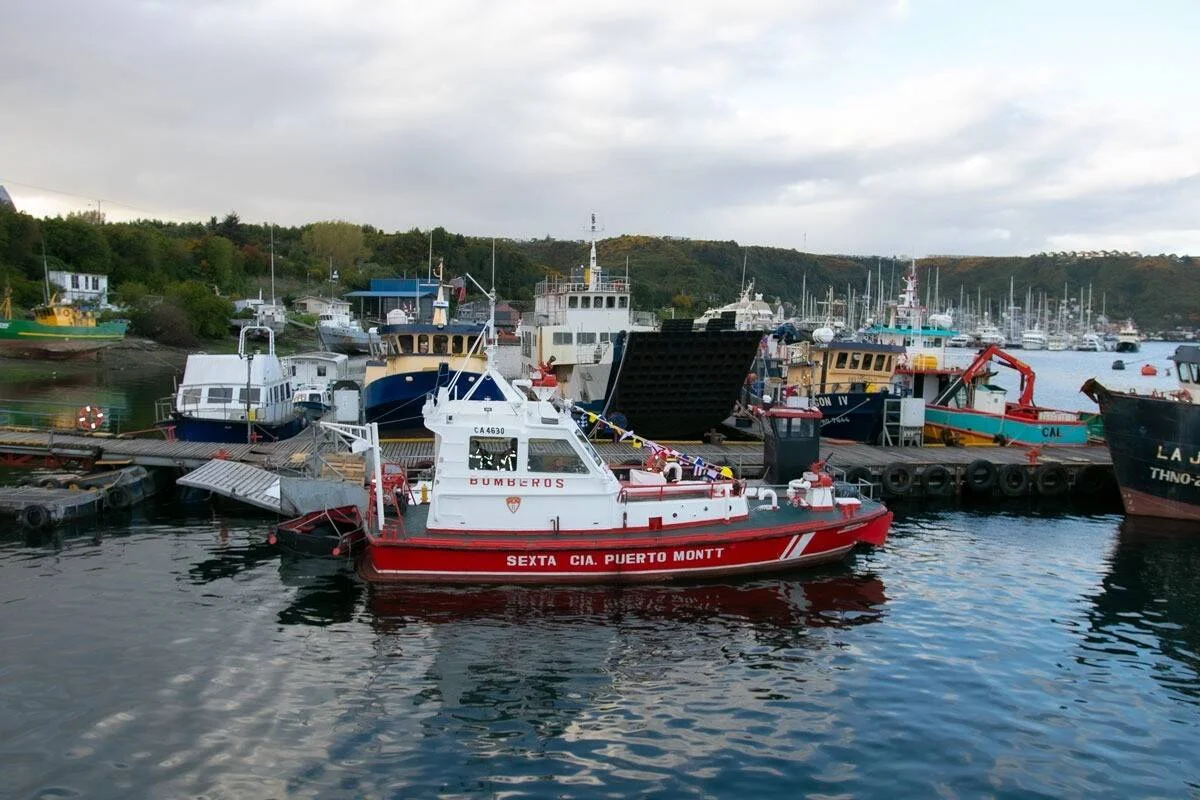 Lancha roja de Bomberos de la Sexta Compañía de Puerto Montt amarrada en el puerto, rodeada de embarcaciones pesqueras.