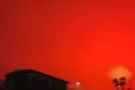 Cielo teñido de rojo intenso sobre siluetas de edificios y palmeras, posiblemente por incendios o fenómeno atmosférico.