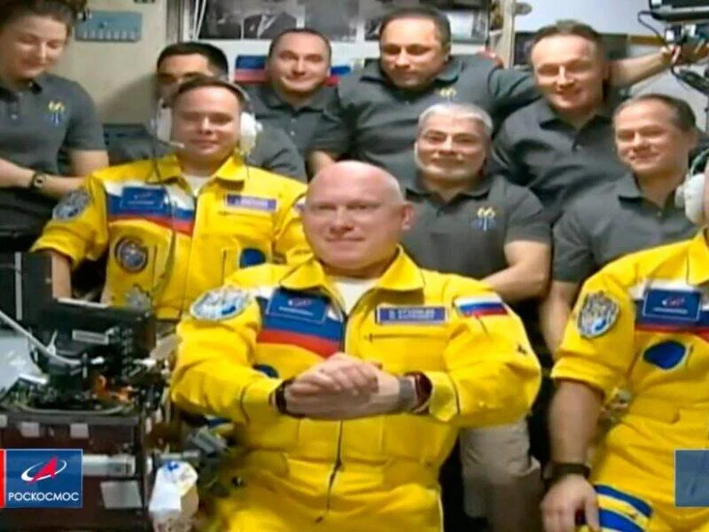 Tres cosmonautas rusos con trajes amarillos y azules posan junto a otros tripulantes a bordo de la Estación Espacial Internacional.