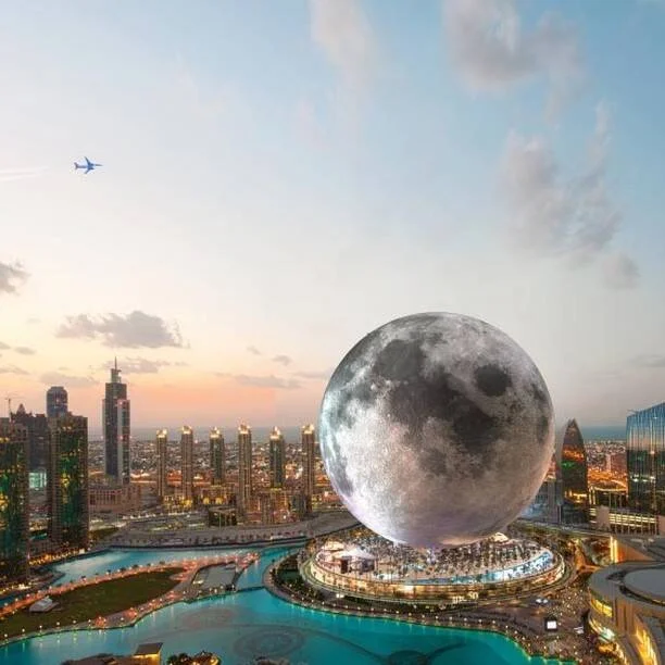 Render de un enorme edificio esférico con apariencia de luna llena sobre el horizonte urbano de Dubái al atardecer.