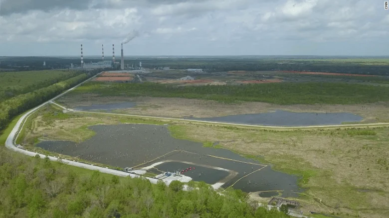 Vista aérea de una planta industrial con chimeneas y grandes balsas de residuos líquidos rodeadas de vegetación.