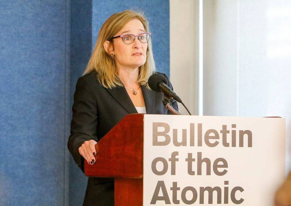 Una mujer con anteojos y saco oscuro habla en un podio del Bulletin of the Atomic Scientists ante un micrófono.