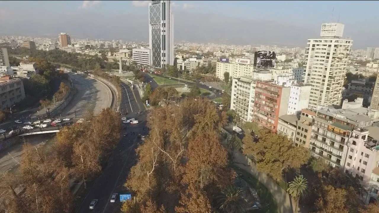 Vista aérea de una amplia avenida con árboles otoñales, edificios en altura y tráfico vehicular en una gran ciudad.