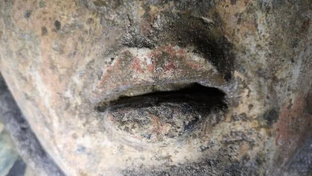 Primer plano de los labios de una escultura antigua de piedra con restos de pigmento rojo visible.