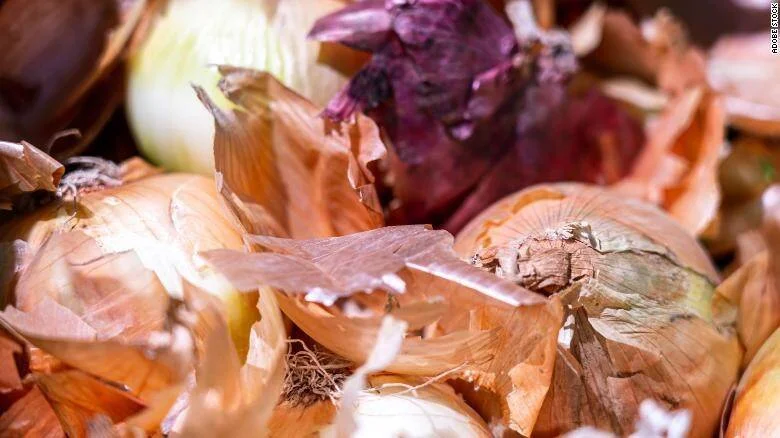Cebollas amarillas y moradas con sus cáscaras secas apiladas en primer plano.