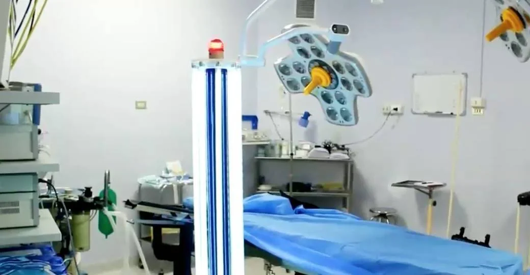 Lámpara de luz ultravioleta para desinfección junto a una camilla quirúrgica y lámpara cialítica en un quirófano.