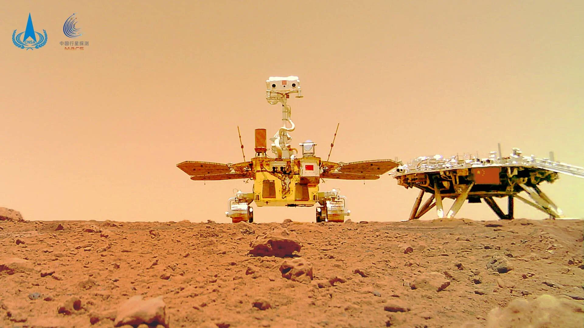 El rover Zhurong de la CNSA posa junto a su plataforma de aterrizaje sobre la superficie rocosa y rojiza de Marte.