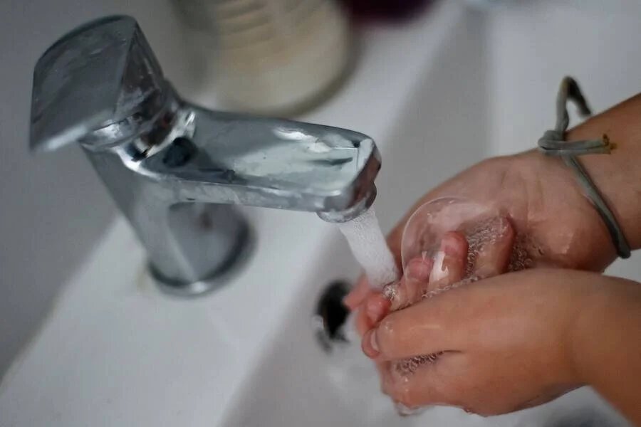 Manos con espuma de jabón enjuagándose bajo el chorro de agua de un grifo cromado.