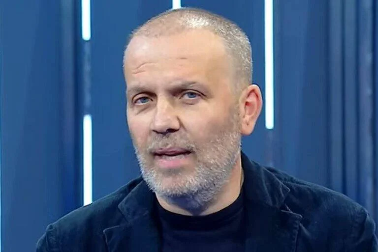 Hombre de mediana edad con cabeza rapada y barba canosa habla frente a cámara en un estudio de televisión con fondo azul.