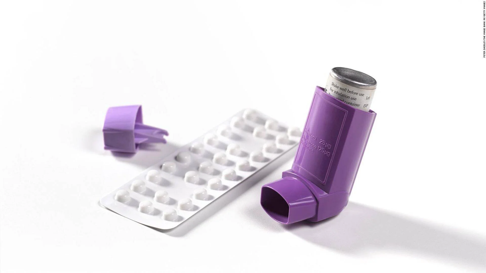 Inhalador de dosis medida color violeta junto a un blíster de pastillas blancas sobre fondo blanco.