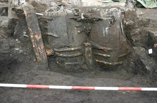 Dos grandes barriles de madera degradados hallados durante una excavación arqueológica en suelo oscuro.
