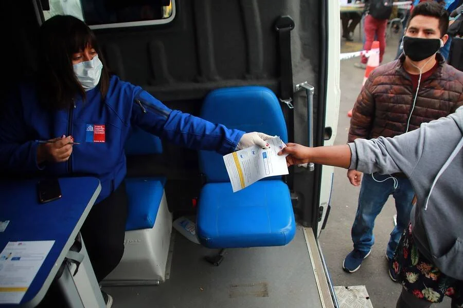 Funcionaria con mascarilla y guantes entrega un documento a una persona desde el interior de una unidad móvil del Ministerio de Salud de Chile.