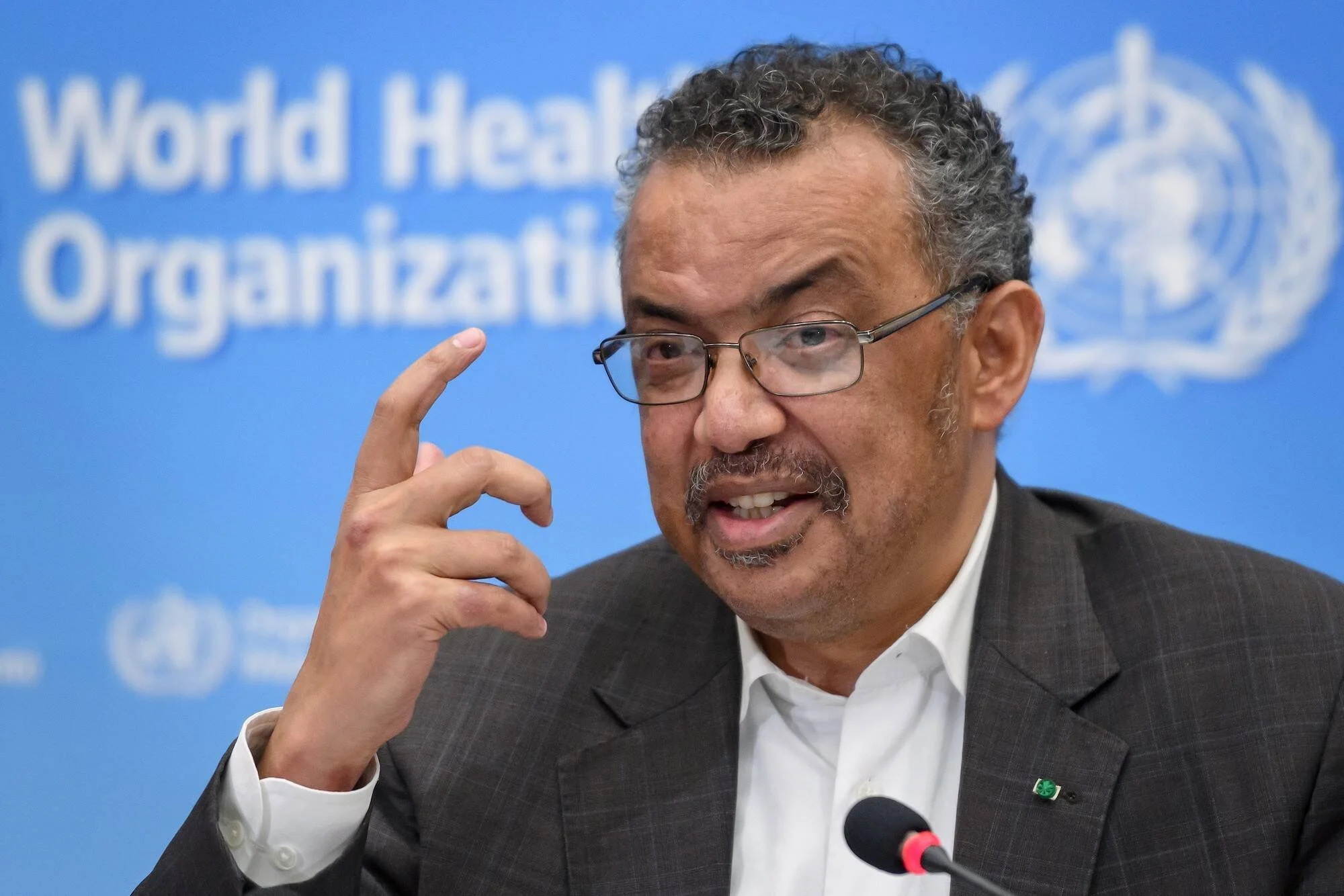 Hombre con anteojos gesticula mientras habla en una conferencia de prensa ante el logo de la Organización Mundial de la Salud.