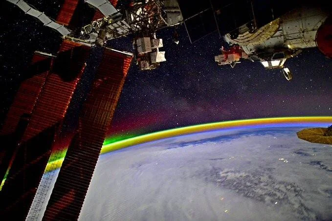 Vista desde la Estación Espacial Internacional mostrando una aurora boreal multicolor sobre la curvatura de la Tierra, con paneles solares en primer plano.