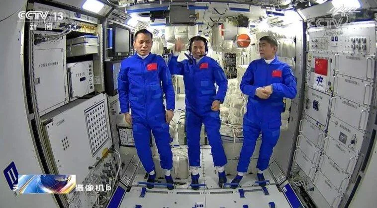 Tres taikonautas con trajes azules y bandera china posan dentro del módulo de la estación espacial Tiangong, transmitido por CCTV 13.