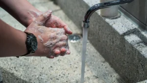 Persona enjabonándose las manos con espuma bajo el chorro de agua de un grifo metálico, con reloj en la muñeca.