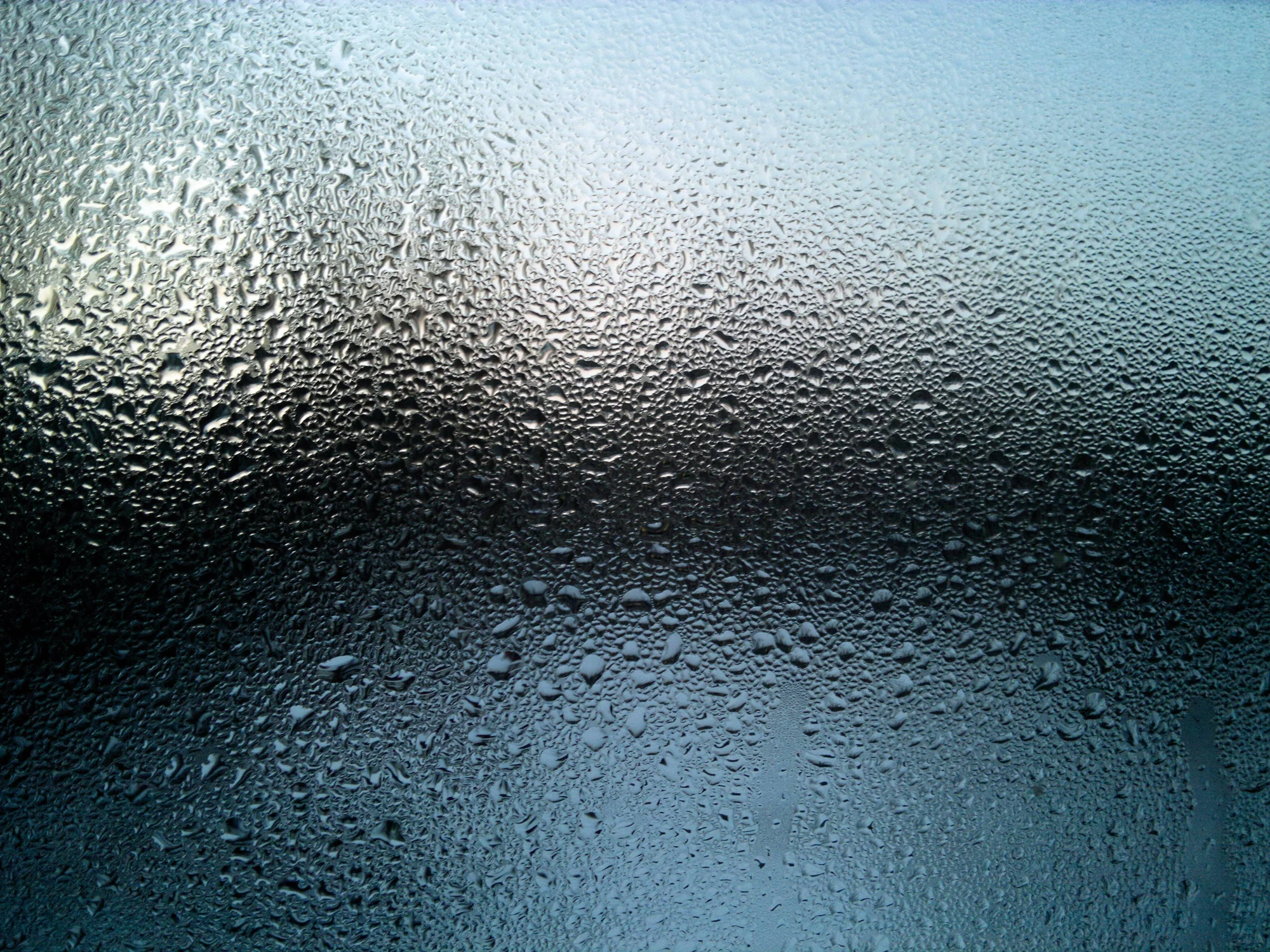 Gotas de condensación cubren un vidrio empañado con tonos grises y azulados al fondo.