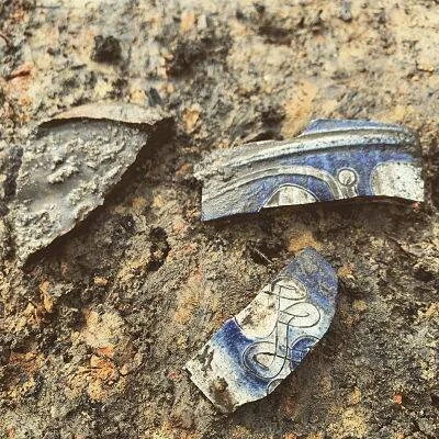 Tres fragmentos de cerámica antigua con decoración azul y blanca sobre superficie de tierra rojiza.