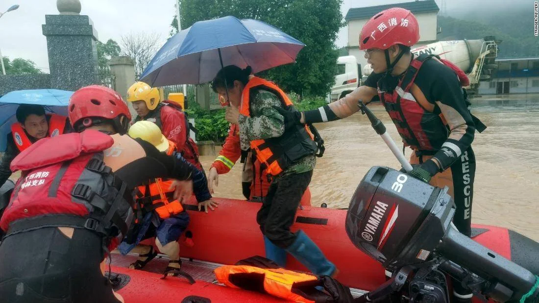 Bomberos de Guangxi ayudan a civiles a subir a bote de rescate en zona inundada bajo la lluvia.