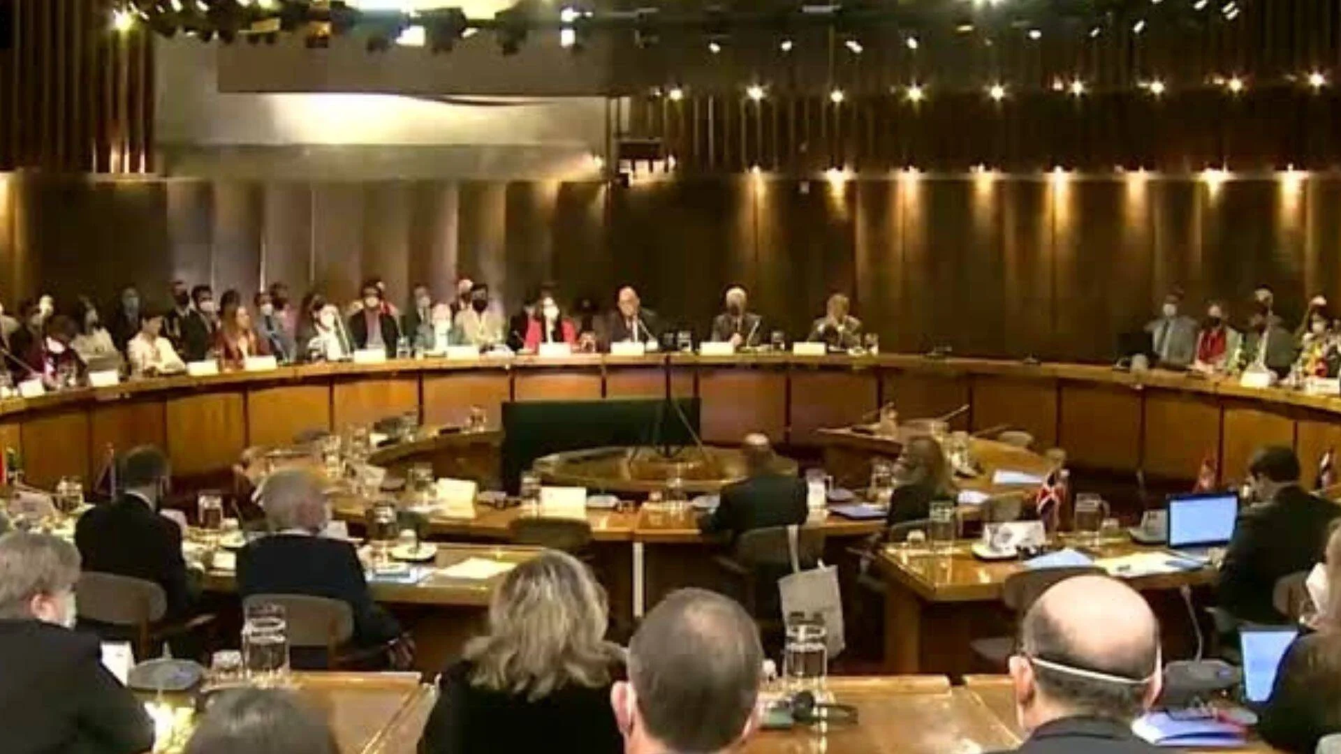 Numerosos delegados reunidos alrededor de una gran mesa redonda en un salón de conferencias de alto nivel.