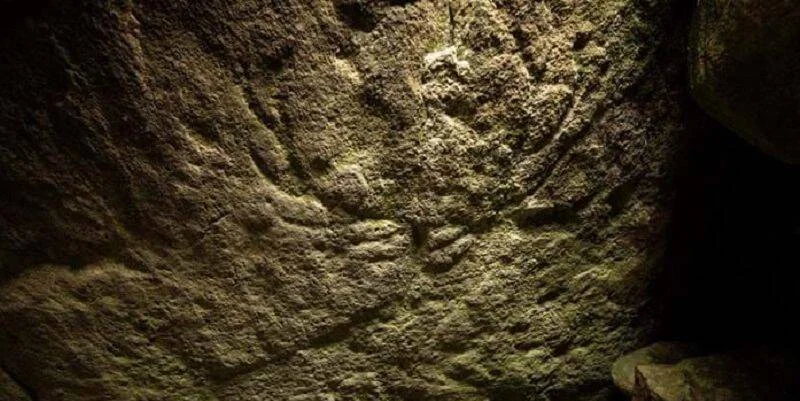 Grabado rupestre con forma de menorá tallado en una roca iluminada en un entorno oscuro.