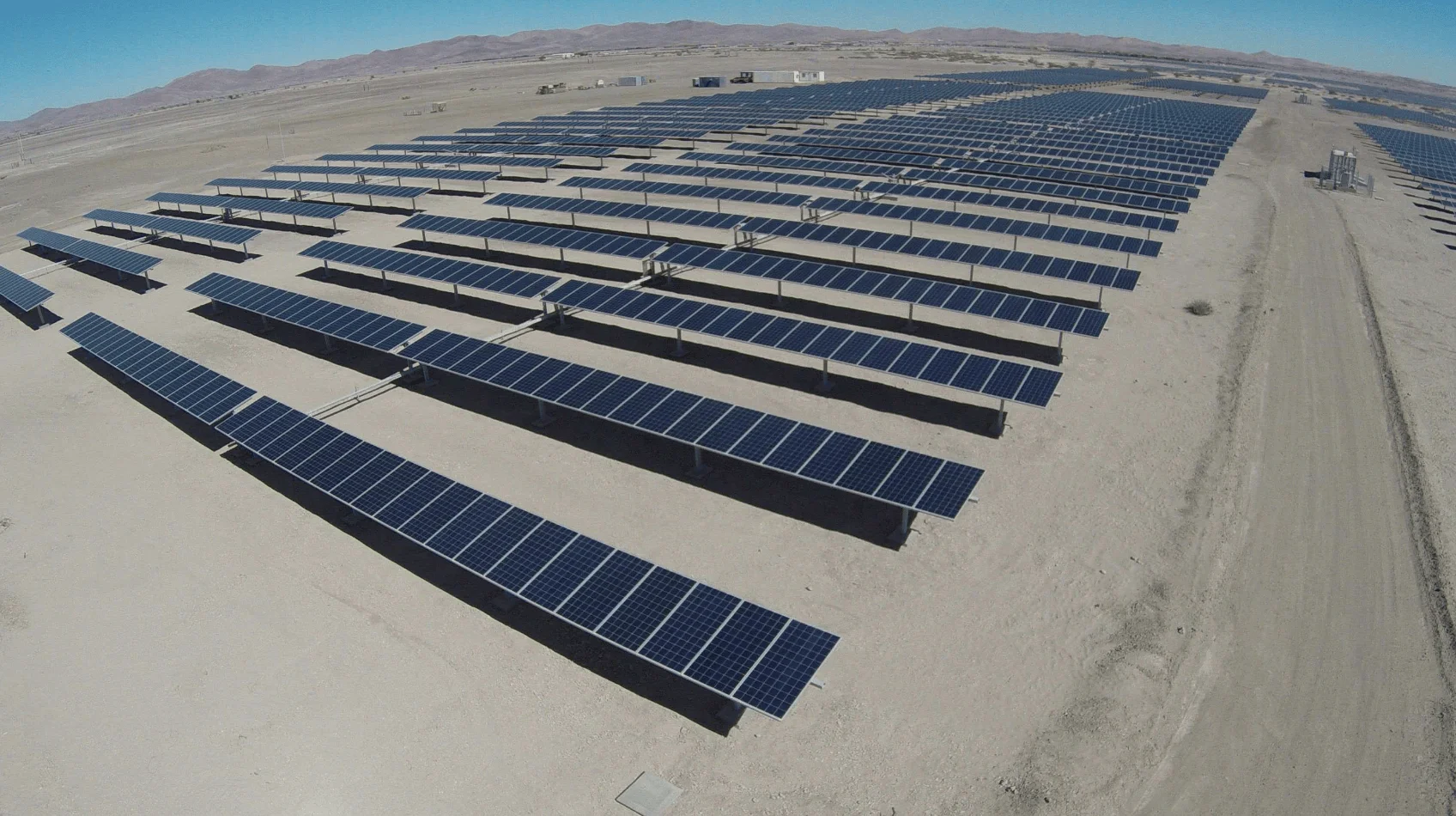 Vista aérea de un extenso parque solar con cientos de paneles fotovoltaicos instalados en un terreno desértico árido.