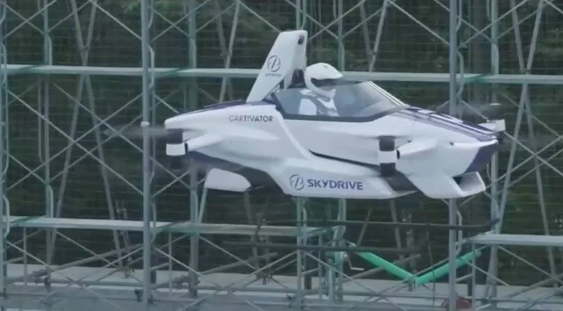 Vehículo volador eléctrico de SkyDrive y Cartivator con un piloto a bordo elevándose dentro de una estructura de seguridad durante una prueba.