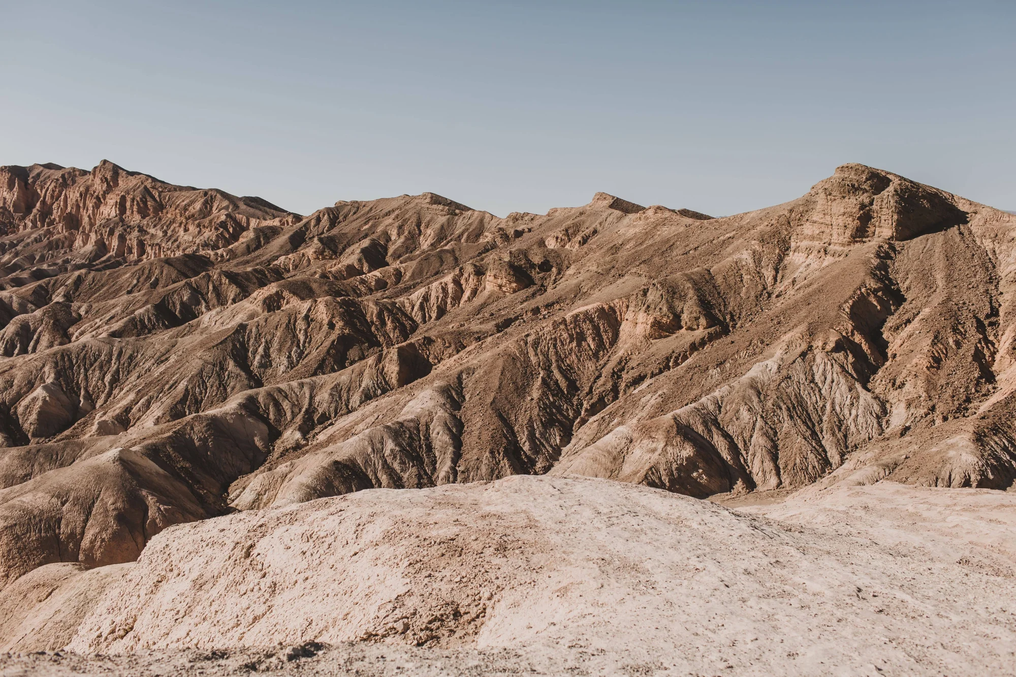 Paisaje desértico árido con colinas erosionadas de tonos ocres y marrones bajo un cielo despejado.