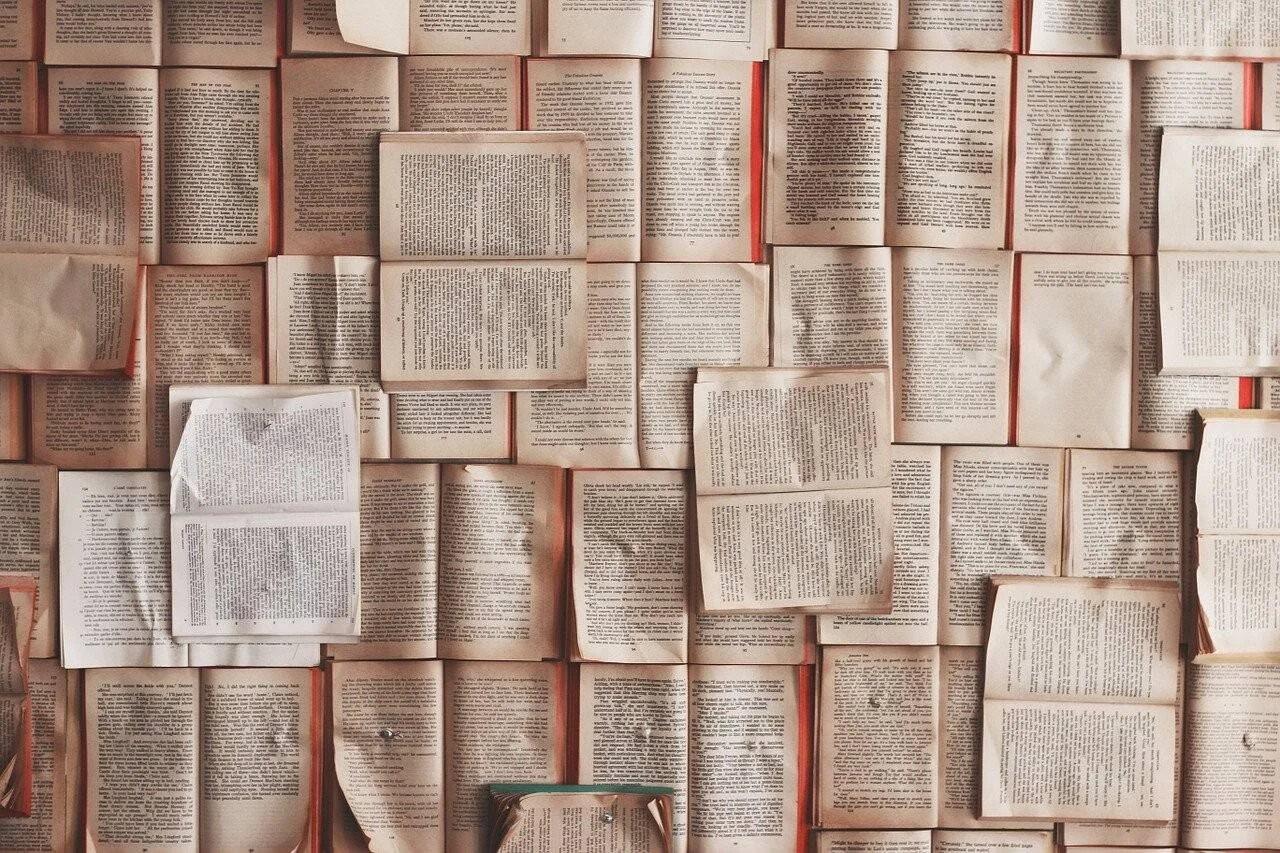 Decenas de libros abiertos colocados juntos formando una superficie cubierta completamente de páginas con texto impreso.