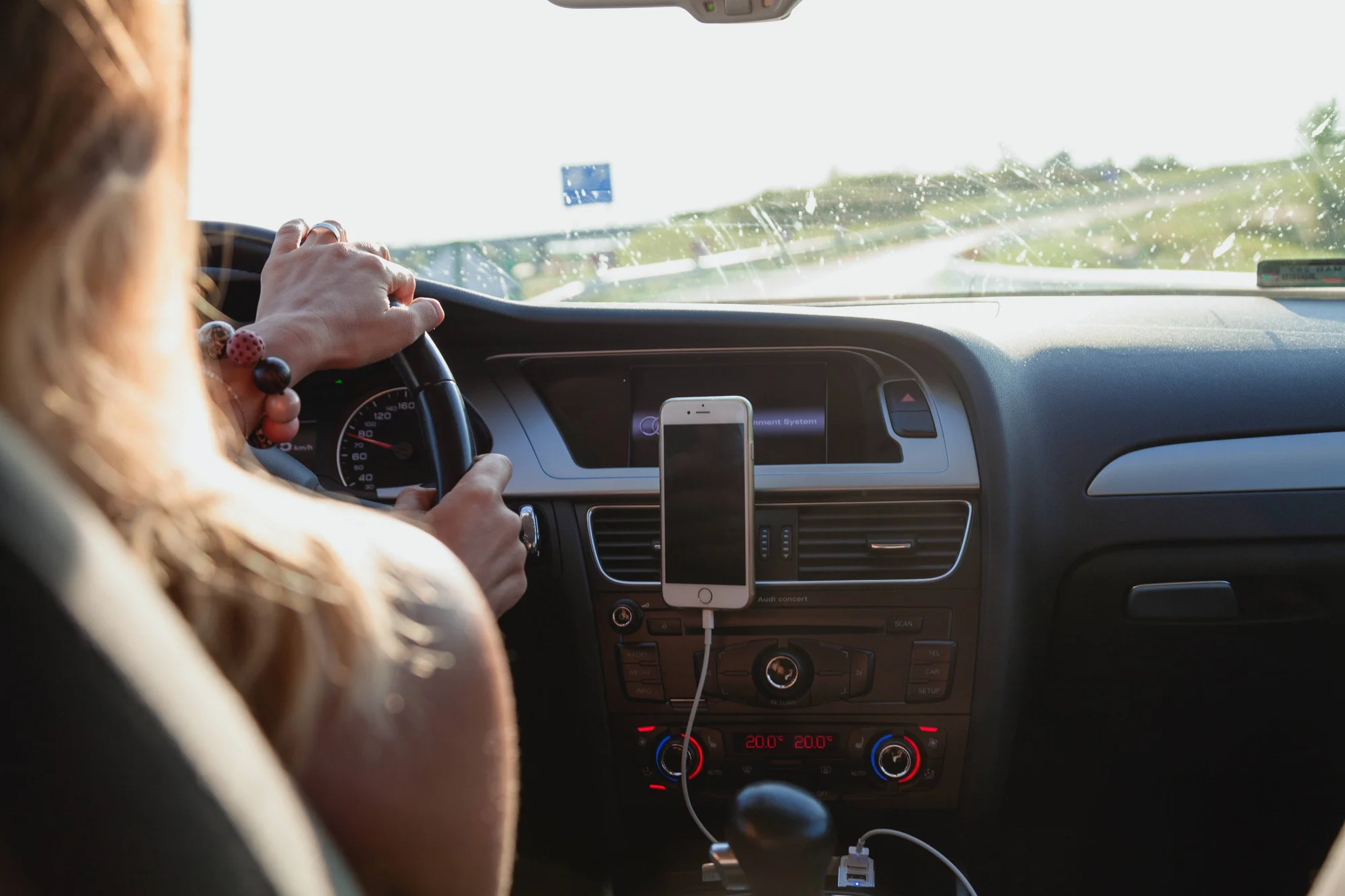 Mujer conduce un automóvil por autopista con un teléfono inteligente sujeto al tablero mediante soporte.