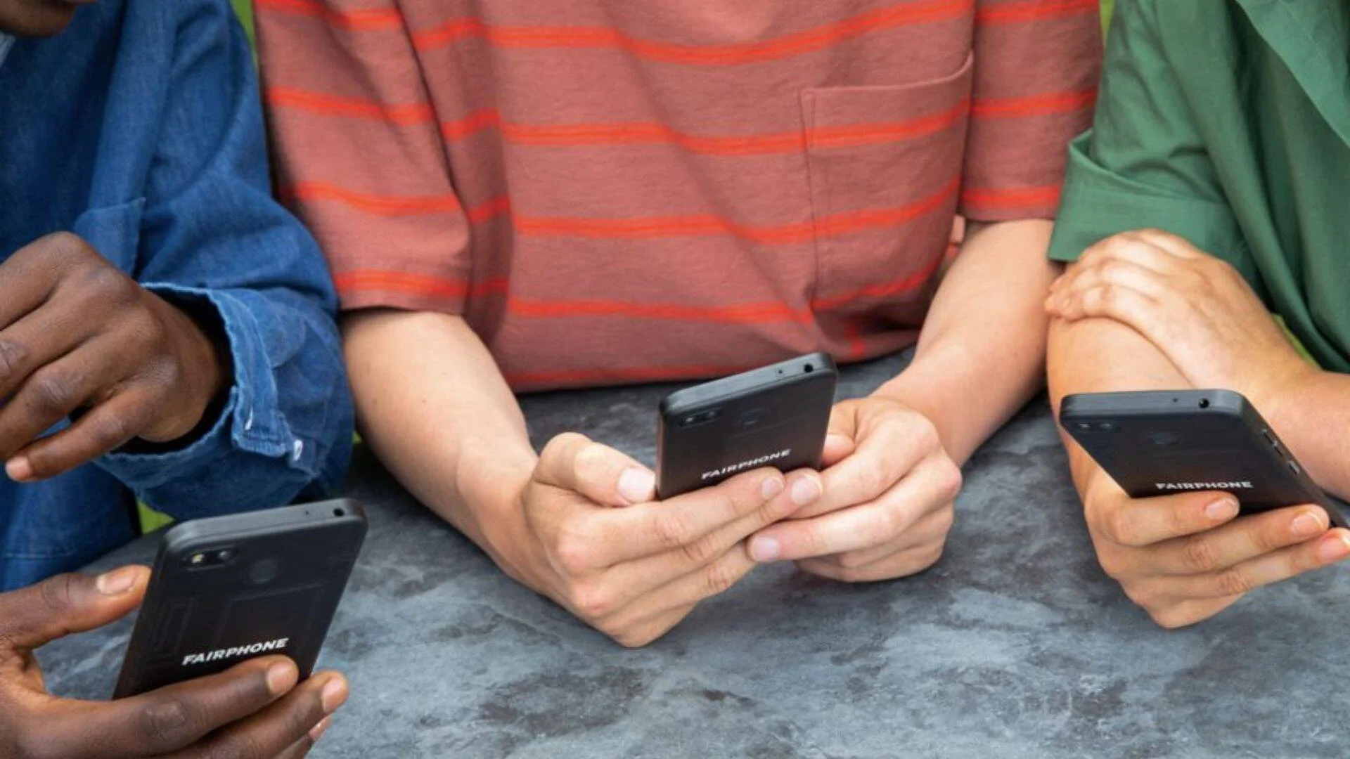 Tres personas sostienen cada una un teléfono inteligente de la marca Fairphone visto por la parte trasera.