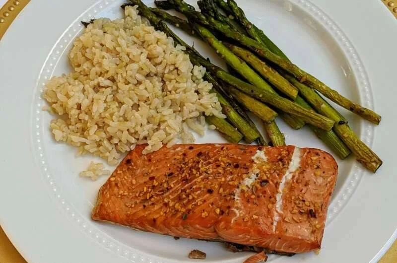 Filete de salmón horneado con especias, arroz integral y espárragos asados servidos en un plato blanco.