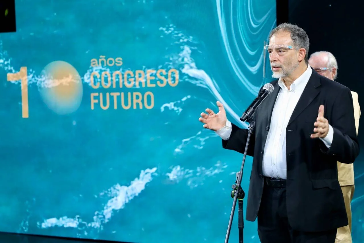 Hombre habla ante un micrófono frente a una pantalla que conmemora los 10 años del Congreso Futuro.