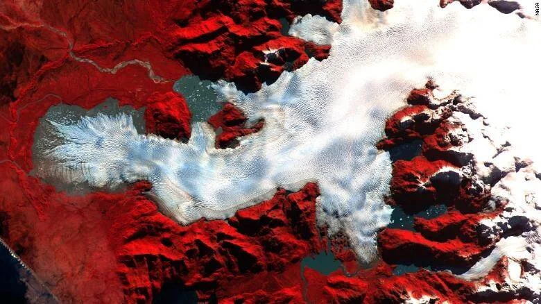 Vista satelital en falso color de la NASA que muestra un lago congelado rodeado de montañas rocosas en tonos rojos y blancos.