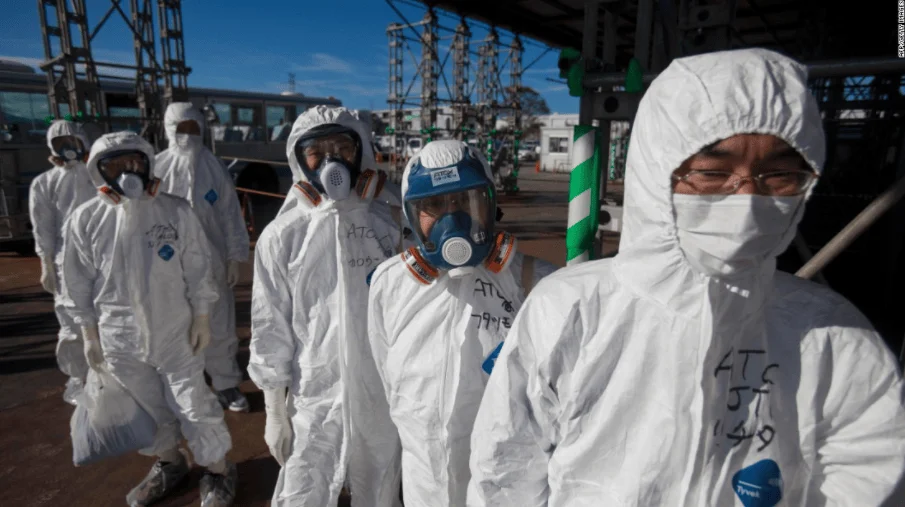 Grupo de trabajadores vestidos con trajes blancos de protección y máscaras respiratorias en instalación nuclear industrial.