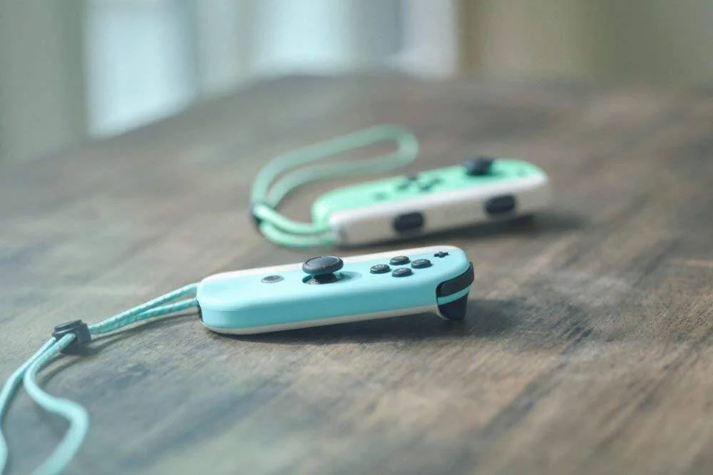 Dos mandos Joy-Con en colores celeste y verde pastel apoyados sobre una mesa de madera con sus correas.