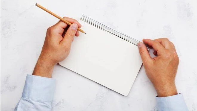 Una persona sostiene un lápiz sobre un cuaderno de espiral en blanco, lista para escribir o dibujar.