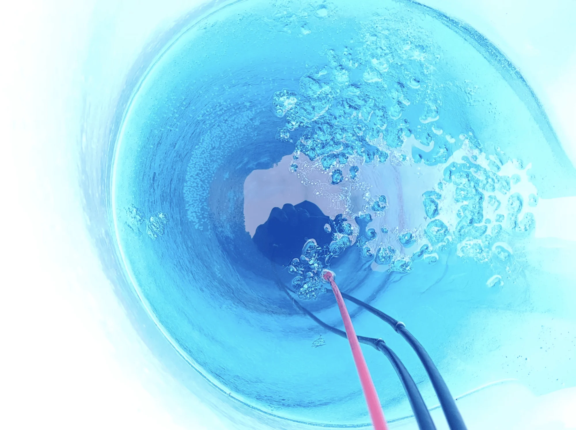 Electrodos rojo y negro sumergidos en agua producen burbujas durante un proceso de electrólisis visto desde arriba.