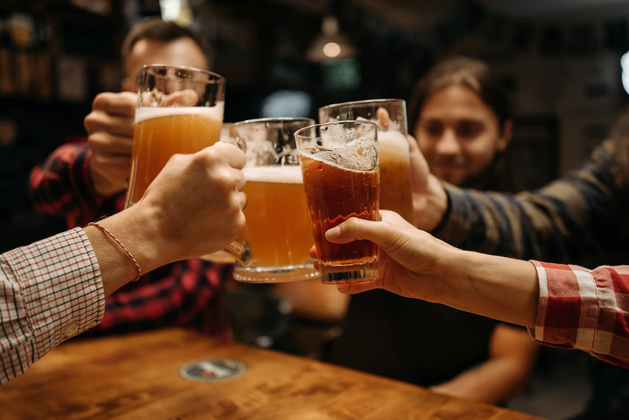Varias personas chocan vasos de cerveza en un brindis sobre una mesa de madera en un bar.