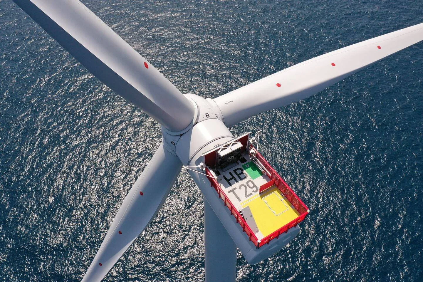 Vista aérea cenital de una turbina eólica offshore con góndola marcada HB T29 sobre el mar abierto.