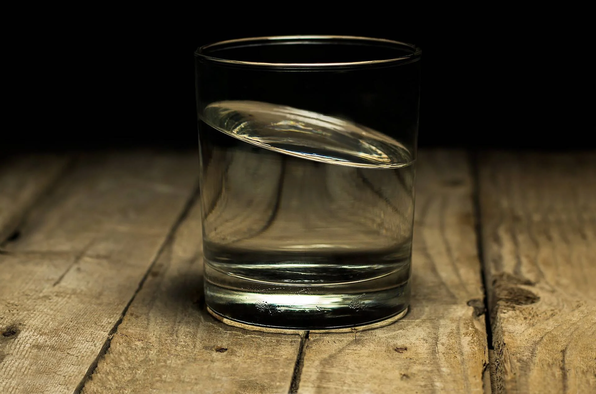 Vaso transparente con agua sobre una mesa de madera rústica con fondo oscuro.