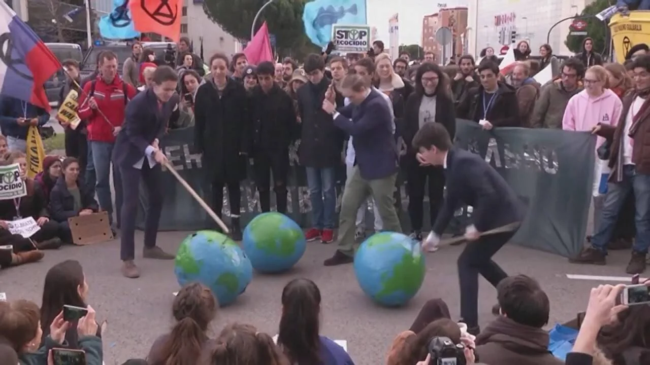 Manifestantes golpean esferas con forma de globo terráqueo durante una protesta por el clima ante una multitud con pancartas de Stop Ecocidio.