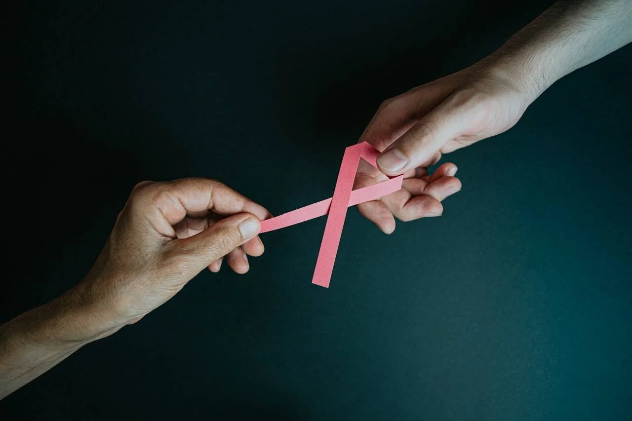 Dos manos sostienen juntas un lazo rosa, símbolo de la lucha contra el cáncer de mama.