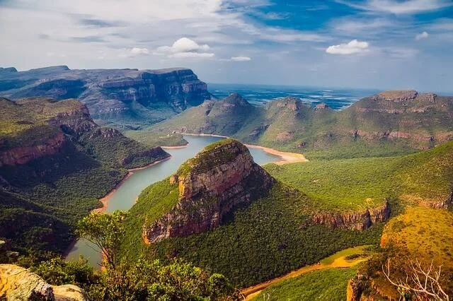 Vista aérea del Cañón del río Blyde con un embalse turquesa rodeado de montañas rocosas cubiertas de vegetación verde bajo cielo azul.