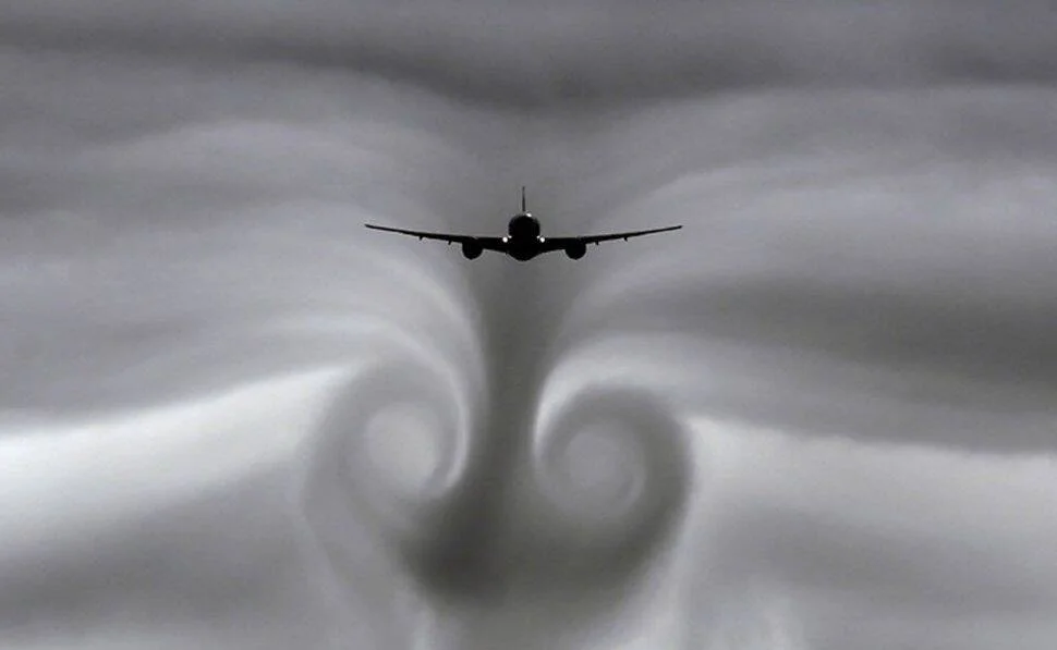 Avión comercial visto desde atrás generando dos grandes vórtices de estela turbulenta visibles en las nubes.